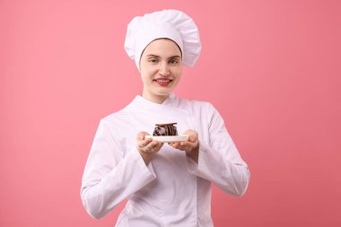 Üniformalı şekerci pembe arka planda çikolatalı tatlı tutuyor.