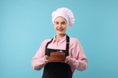 Açık mavi arka planda lezzetli çikolatalı pasta yapan bir pastacı.