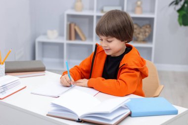 İçeride masa başında ödev yapan sevimli küçük çocuk.