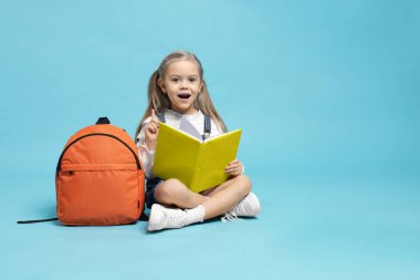 Sırt çantası ve açık mavi arka plan kitabı olan tatlı bir kız öğrenci. Metin için boşluk