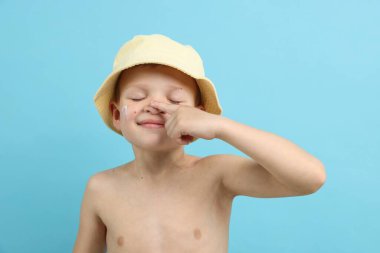 Küçük çocuk açık mavi arka planda cildine güneş kremi sürüyor.