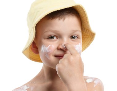 Küçük çocuk beyaz arka planda cildine güneş kremi sürüyor.