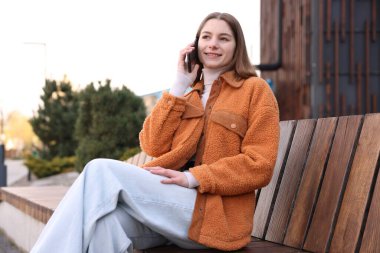 Güzel genç kız dışarıda telefonla konuşuyor.