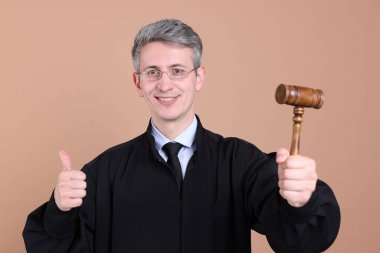 Elinde tokmakla gülümseyen yargıç bej arka planda başparmak gösteriyor