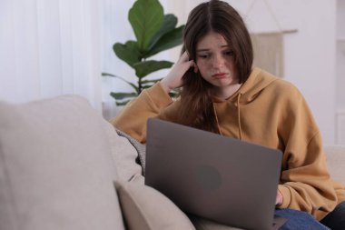 Siber zorbalık. Evdeki kanepede dizüstü bilgisayarı olan üzgün bir genç kız.