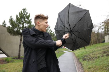 Kırık şemsiyeli bir adam açık havada yağmur altında rüzgarla savaşıyor.