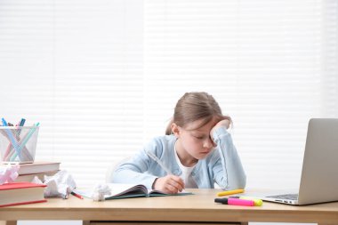 Evde, masada ödev yapmaktan yorulmuş küçük kız.