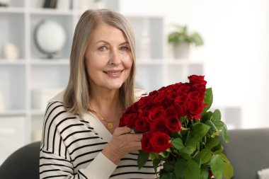 Evdeki kanepede gül buketiyle gülümseyen kadın.