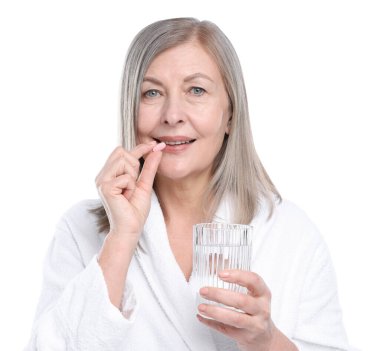 Bir bardak suyla gülümseyen kadın beyaz arka planda kolajen hapı alıyor.