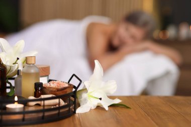 Üst düzey kadın masaj koltuğunda dinleniyor, farklı spa ürünlerine ve zambak çiçeklerine odaklanıyor.