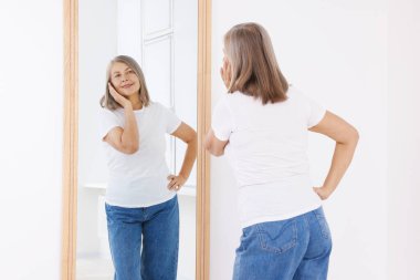 Güzel son sınıf öğrencisi kadın aynada kendine bakıyor.