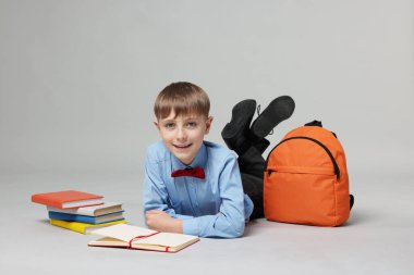 Sırt çantası açık gri arka planda kitap okuyan sevimli bir okul çocuğu.