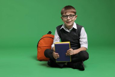 Sırt çantası ve yeşil arka plan kitapları olan tatlı bir okul çocuğu.