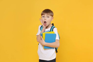 Sırt çantası ve turuncu arka plan kitapları olan tatlı bir okul çocuğu.