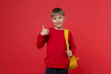 Sırt çantalı yakışıklı okul çocuğu kırmızı arka planda baş parmak gösteriyor.