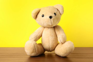 Tahta masada sarı arka planda sevimli bir oyuncak ayı.