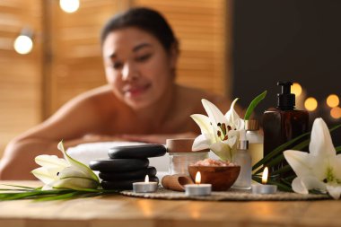 Güzel bir kadın masaj koltuğunda dinleniyor, farklı spa ürünlerine ve zambak çiçeklerine odaklanıyor.