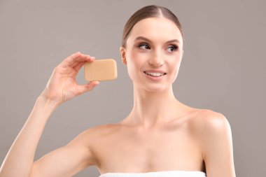 Gri arka planda sabun çubuğuyla gülümseyen kadın.