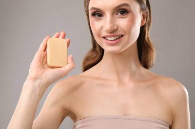 Gri arka planda sabun çubuğuyla gülümseyen kadın, yakın plan.