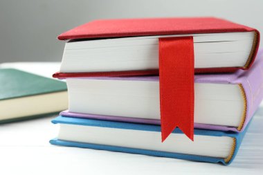 Kırmızı kurdele yer imi ve beyaz ahşap masa üzerinde renkli kitap gri arkaplan, yakın plan