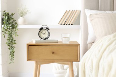 Alarmlı komodinli komodin, bir bardak su ve yatağın yanında kitap.