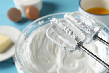 Açık mavi masada çırpılmış krema ve çırpılmış kremayla karıştırıcı, yakın plan.