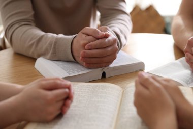 İncilli aile ahşap masada dua ediyor, yakın plan.