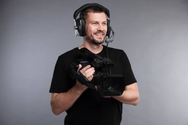 Profesyonel kameralı ve kulaklıklı bir adam gri arka planda.
