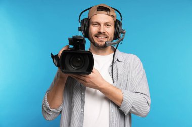 Profesyonel video kamerası ve açık mavi arka planda kulaklığı olan bir adam.