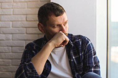 Evdeki pencerenin yanında oturan depresif bir adam.