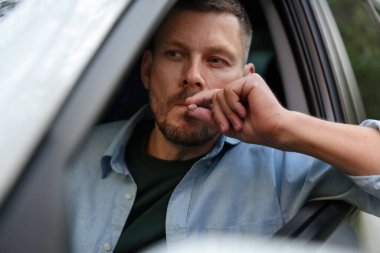 Arabada sigara içen bir adam, dışarıdan manzaralı.