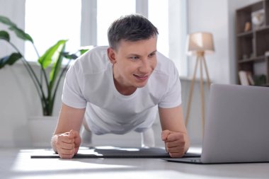 Evde bilgisayarla yoga dersi alan bir adam.