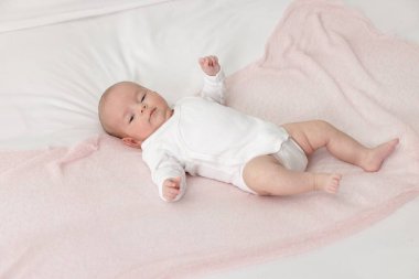 Sevimli küçük bebek evde yatakta yatıyor, manzaranın üstünde.