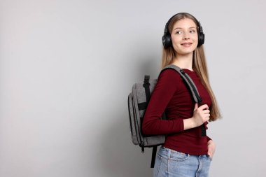 Açık gri arka planda kulaklığı ve sırt çantası olan genç bir kız. Metin için boşluk