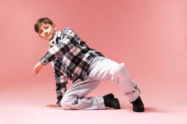 Kulaklıklı, şık elbiseli, pembe arka planda dans eden bir çocuk.