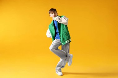 Şık giyinmiş çocuk turuncu arka planda dans ediyor.