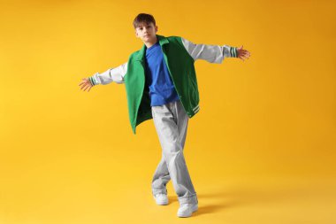 Şık giyinmiş çocuk turuncu arka planda dans ediyor.