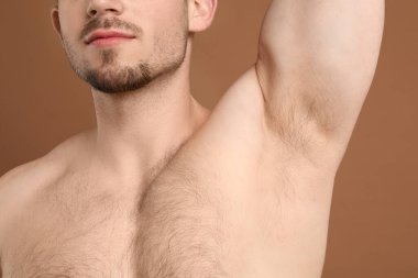 Genç adam kahverengi arka planda kıllı koltuk altlarını gösteriyor, yakın plan. Epilasyon işlemi