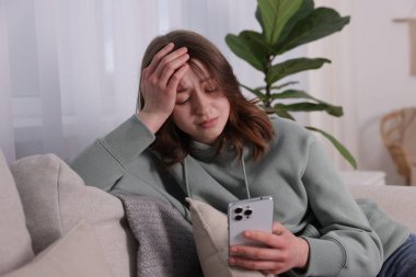 Siber zorbalık. Evdeki kanepede akıllı telefonlu üzgün genç kız.