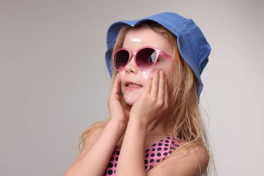 Yüzünde güneş kremi olan sevimli küçük bir kız. Gri arka planda, yakın plan.