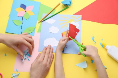 Anne ve kızı sarı masada el yapımı bir proje yapıyor.