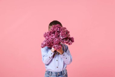 Pembe arka planda bir buket leylak çiçekli küçük çocuk.