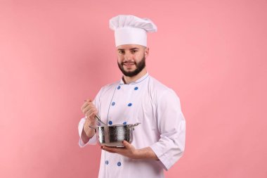 Üniformalı mutlu pastacı elinde çırpıcı ve pembe arka planda pişirme kabı tutuyor.