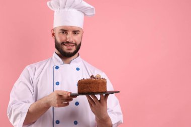 Üniformalı mutlu pastacı pembe arka planda çikolatalı pasta tutuyor