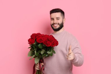 Pembe arka planda kırmızı güller açan mutlu bir adam.