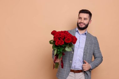 Kırmızı gül buketi olan mutlu adam bej arka planda baş parmağını gösteriyor, mesaj için yer var.