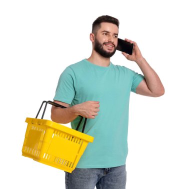 Boş alışveriş sepetli bir adam beyaz arka planda akıllı telefondan konuşuyor.