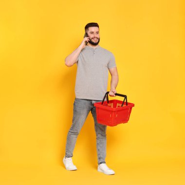 Boş alışveriş sepetli bir adam akıllı telefondan turuncu arka planda konuşuyor.