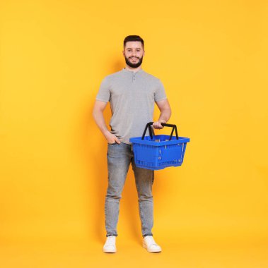 Turuncu arka planda boş alışveriş sepeti olan adam.