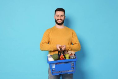 Açık mavi arka planda ürünlerle dolu alışveriş sepeti olan bir adam.